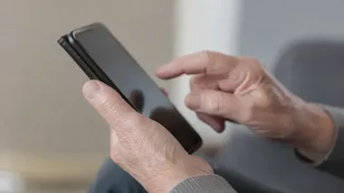 Dłonie starszej osoby trzymającej smartfon i dotykającej ekranu.